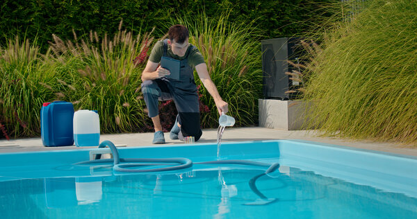 Ein Pooltechniker fügt Chemikalien in den Pool hinzu und hält dabei ein Tablet, um die Wasserqualität zu überwachen.